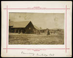 Photograph including several buildings in background with American Indians in foreground.